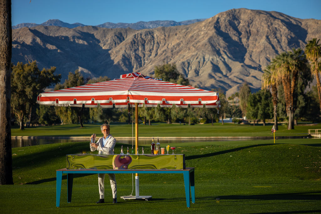 A well-dressed bartender shaking a cocktail on the Desert Island putting green at sunset.